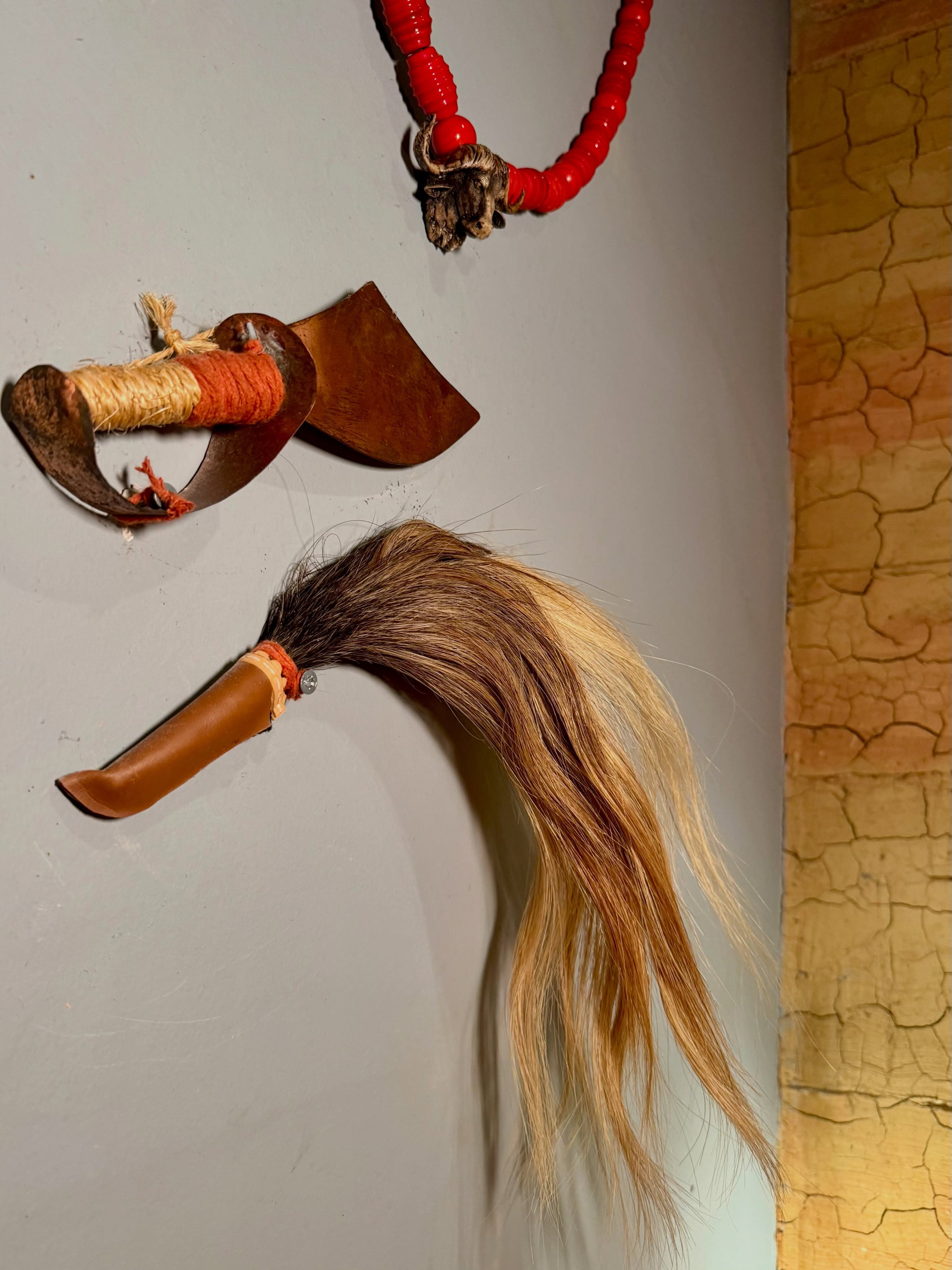 Peça de decoração afro na parede do salão, com fios vermelhos e palha