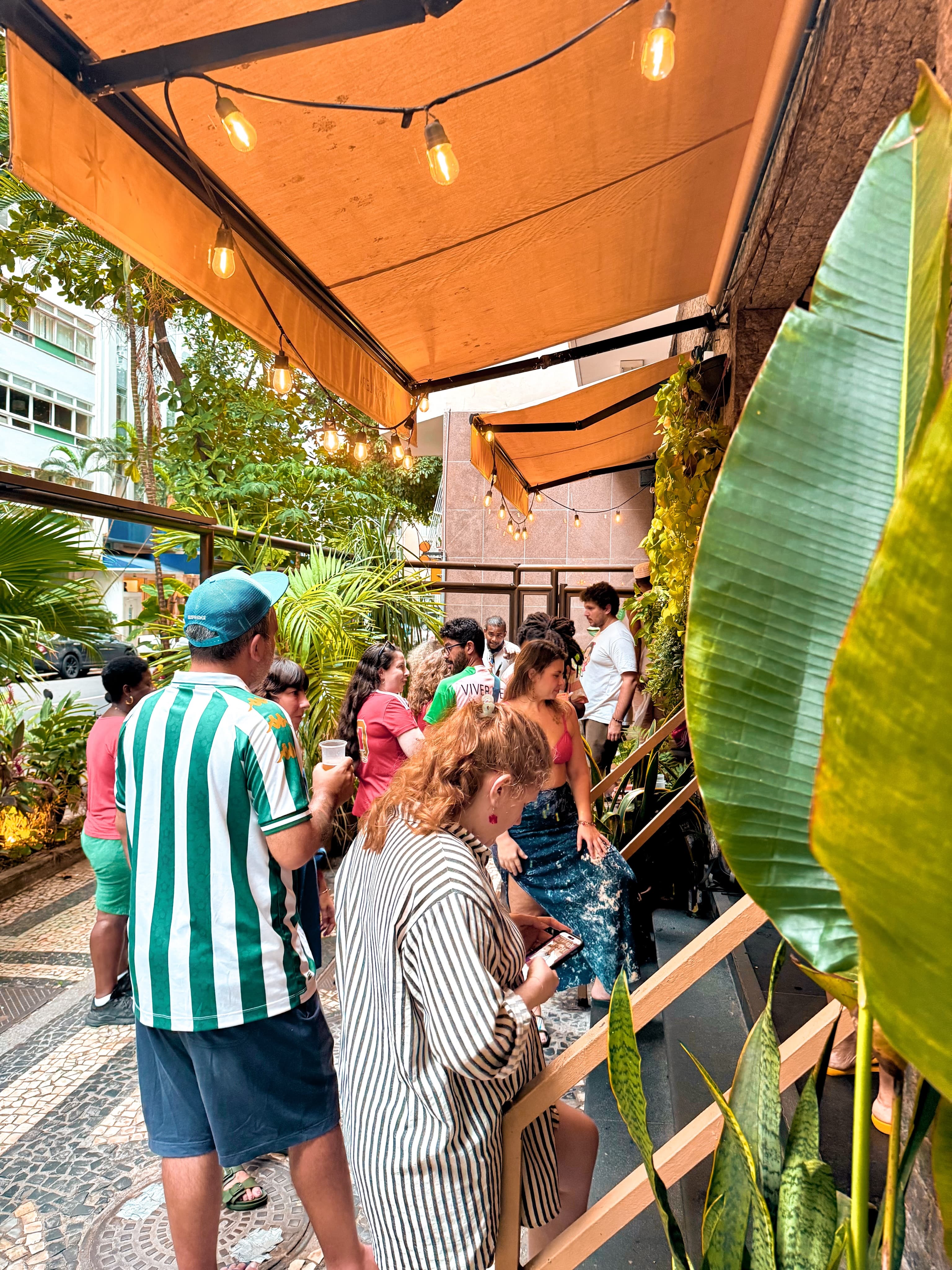 A varanda do Yayá cheia de gente, sob o toldo laranja e as folhas de bananeira